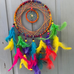 May include: A colorful dreamcatcher with a rainbow of feathers and beads. The dreamcatcher has a circular frame with a smaller circle in the center. The feathers are arranged in a cascade around the dreamcatcher.