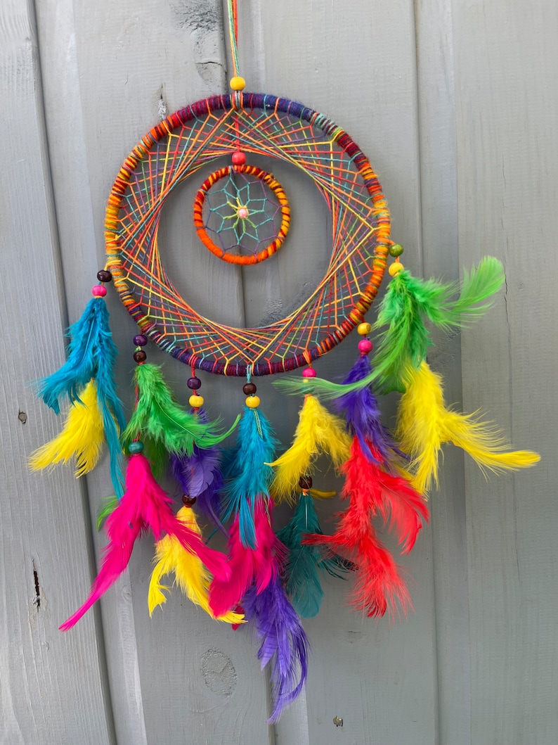 May include: A colorful dreamcatcher with a rainbow of feathers and beads. The dreamcatcher has a circular frame with a smaller circle in the center. The feathers are arranged in a cascade around the dreamcatcher.