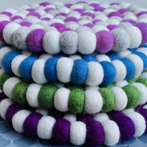 May include: A set of four round felt coasters in purple, green, blue, and grey. Each coaster is made of a circle of felt balls.