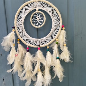 May include: White dream catcher with a white and beige beaded fringe and white feathers. The dream catcher has a smaller white circle in the center.
