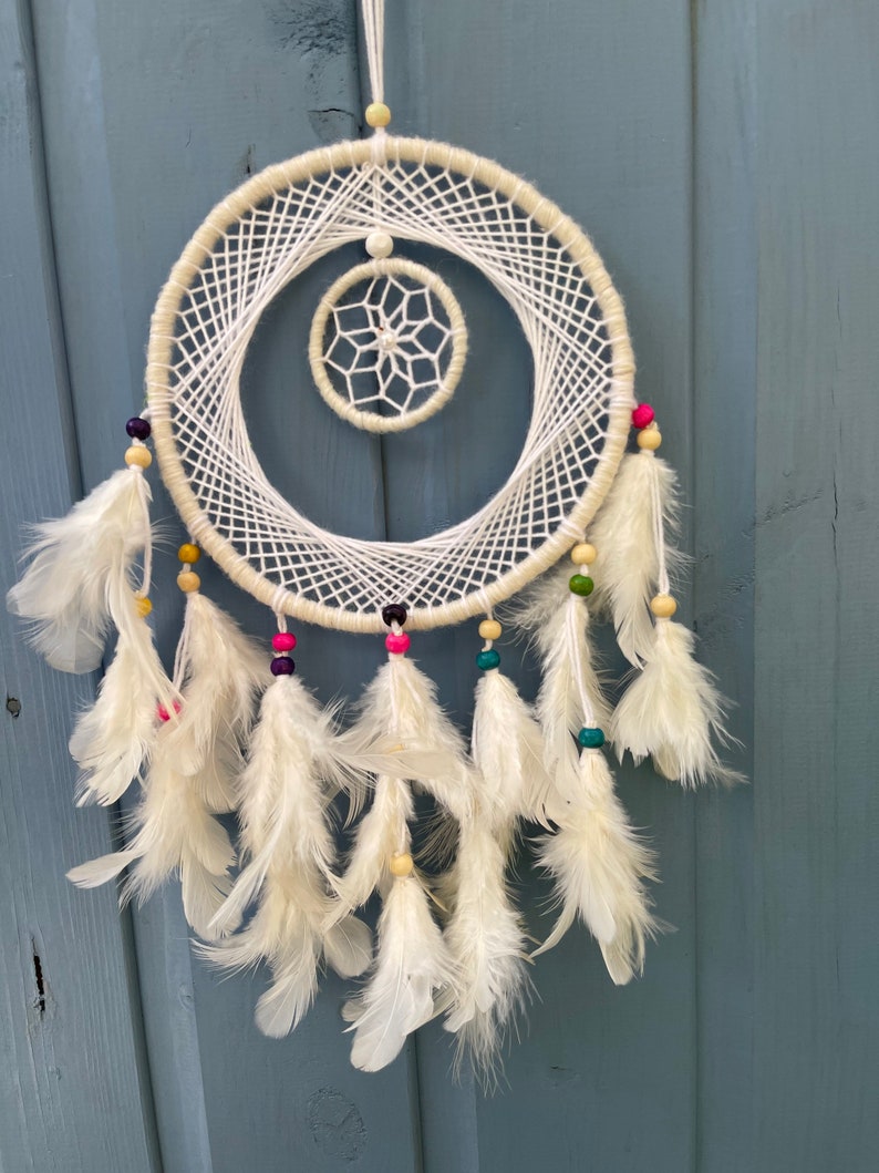 May include: White dream catcher with a white and beige beaded fringe and white feathers. The dream catcher has a smaller white circle in the center.