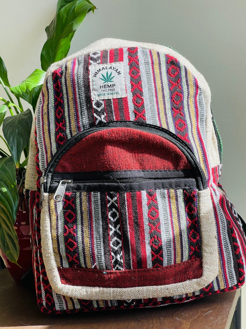 May include: A red, black, white, and yellow striped hemp backpack with a brown leather patch that says "Himalayan Hemp THC Free Made in Nepal".