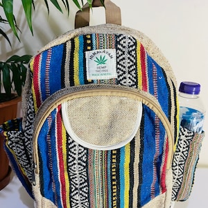May include: A multi-colored striped hemp backpack with a brown leather strap and a small pocket on the side. The backpack has a label that reads "Himalayan Hemp THC Free Made in Nepal".