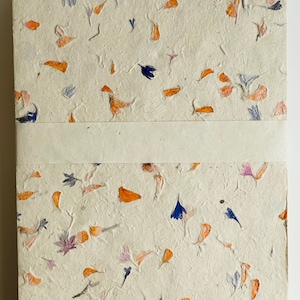 May include: A handmade notebook with a cream-colored cover featuring a unique design of pressed orange, blue, and pink flower petals.