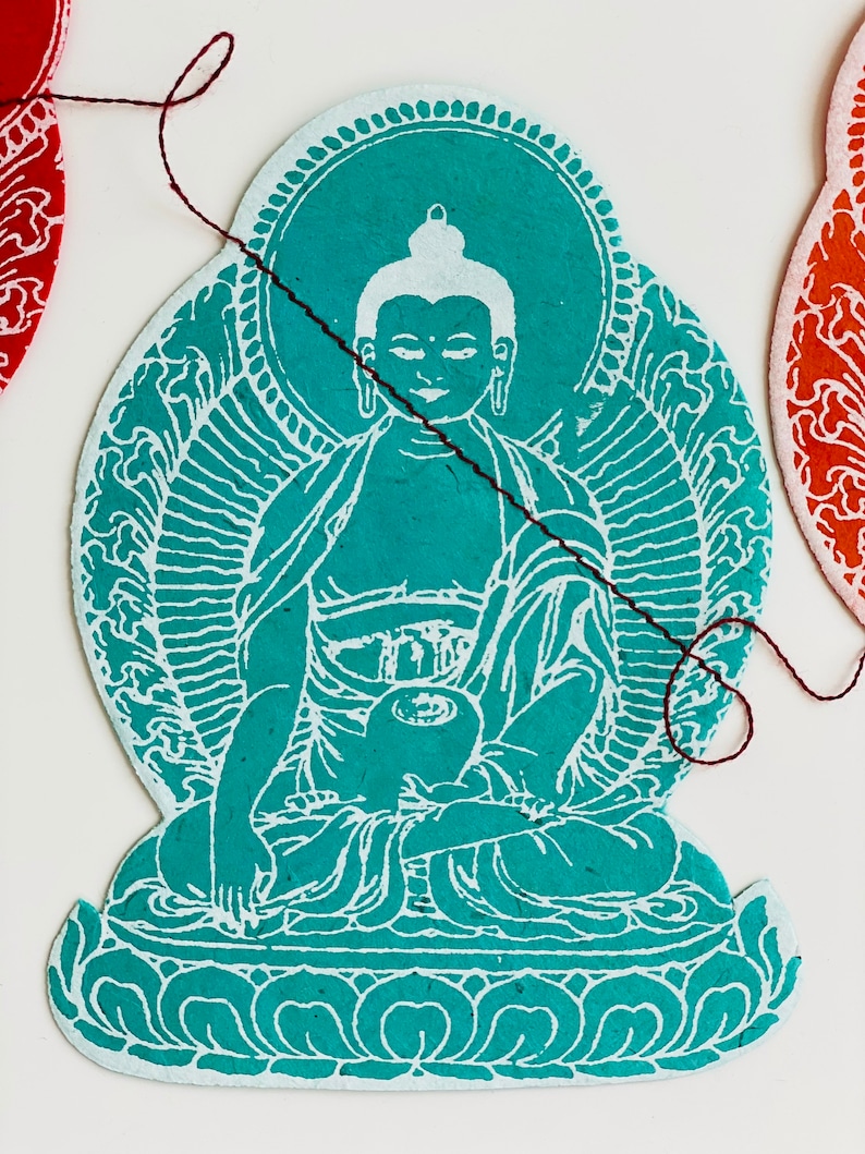 K&ouml;nnte beinhalten: Ein blaugr&uuml;ner Papierschnitt eines sitzenden Buddha mit einem wei&szlig;en Heiligenschein und wei&szlig;en Details. Der Buddha sitzt in meditativer Haltung mit den H&auml;nden im Scho&szlig;.