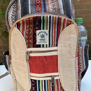 May include: A multi-coloured striped hemp backpack with a large front pocket and two smaller zipped pockets. The backpack has a brown leather zipper pull and a patch that says "Himalayan Hemp THC Free Made in Nepal".