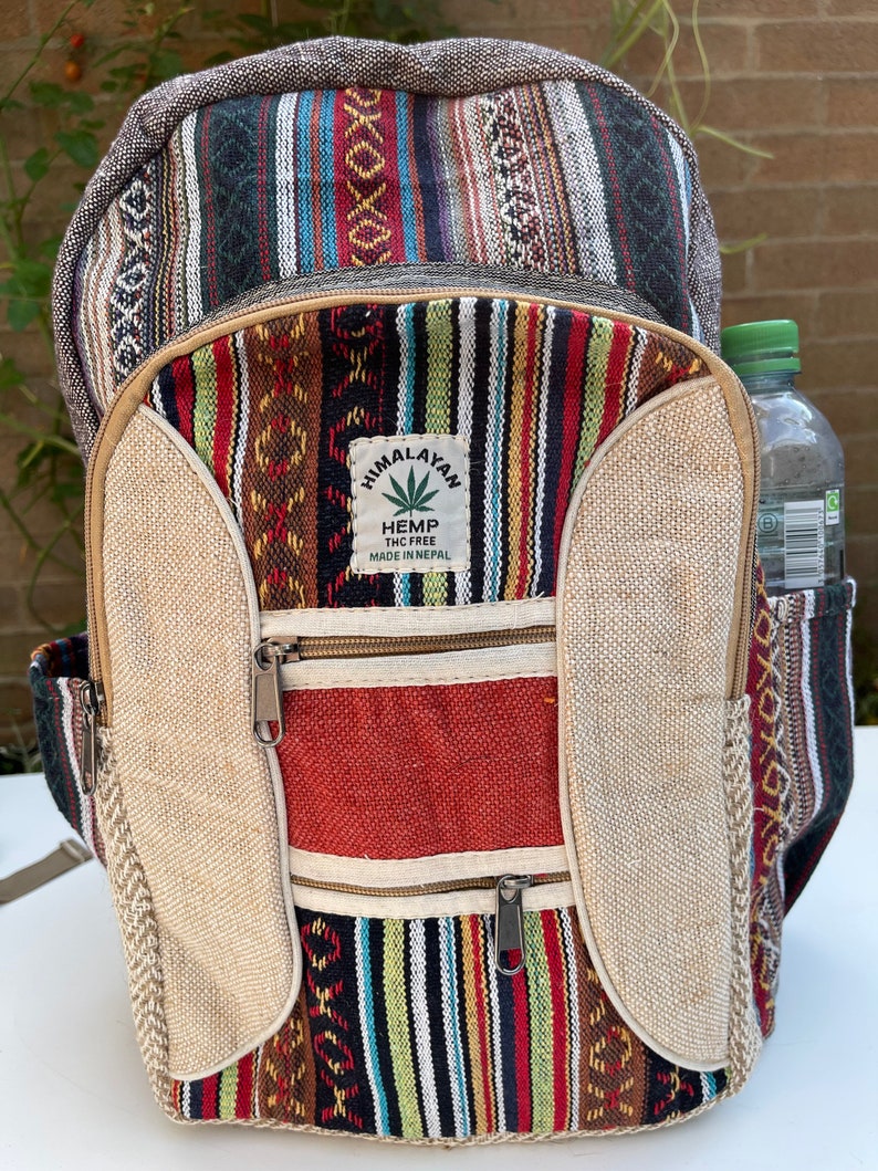 May include: A multi-coloured striped hemp backpack with a large front pocket and two smaller zipped pockets. The backpack has a brown leather zipper pull and a patch that says "Himalayan Hemp THC Free Made in Nepal".