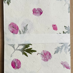 May include: A stack of white paper with pressed pink flower petals and green leaves. The paper has a textured surface.