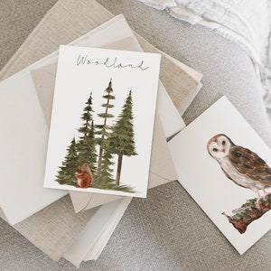 May include: Two watercolor illustrations on white cardstock. The first card features a group of green pine trees with a brown squirrel sitting at the base of the trees. The text "Woodland" is written in black cursive at the top of the card. The second card features a white barn owl with brown markings perched on a branch.