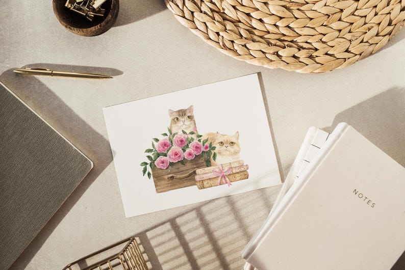 May include: A watercolor illustration of two cats, one gray and one cream-colored, with pink roses. The cats are positioned near a wooden box and books tied with a pink ribbon. The image is on a white card.