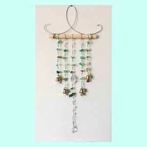 May include: A green glass and metal wind chime with a wooden dowel and a crystal at the bottom. The chime features a tree of life charm and small bells.