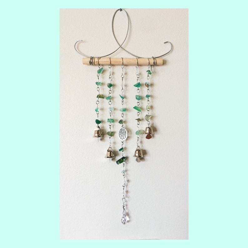 May include: A green glass and metal wind chime with a wooden dowel and a crystal at the bottom. The chime features a tree of life charm and small bells.