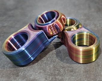 Peut inclure: Trois toupies de fidget irisées dans des tons de bleu, or et violet. Les toupies ont un motif texturé rayé et sont en métal.