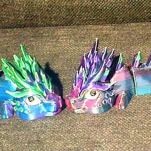 Könnte beinhalten: Zwei bunte, segmentierte Drachen-Schlüsselanhänger. Einer ist blau, grün und lila, der andere ist pink, lila und blau.