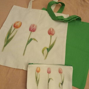 Può includere: Due borse tote in tela bianca con manici verdi. Una borsa ha un pannello laterale verde. Entrambe le borse presentano un design ad acquerello di tulipani rosa e arancioni.