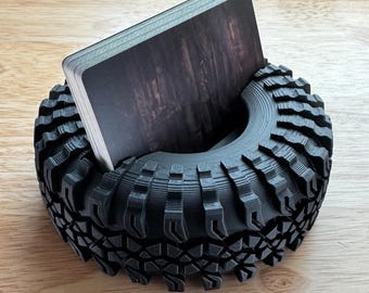 May include: A black 3D printed tyre-shaped card holder with a pack of cards inside.