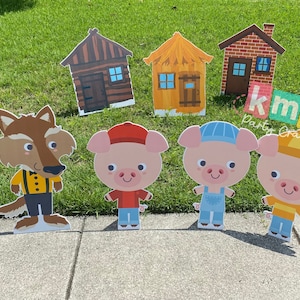 Puede incluir: Un conjunto de siete recortes de cartón con personajes del cuento infantil "Los tres cerditos". El conjunto incluye un lobo, tres cerditos y tres casas. Las casas están hechas de paja, palos y ladrillos. Los recortes son coloridos y tienen un estilo de dibujos animados.
