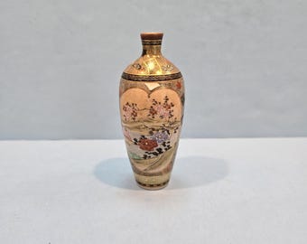 May include: A small, cream-colored ceramic vase with a floral design. The vase has a narrow neck and a wide base. The floral design is in shades of pink, red, and green. The vase is decorated with gold accents.