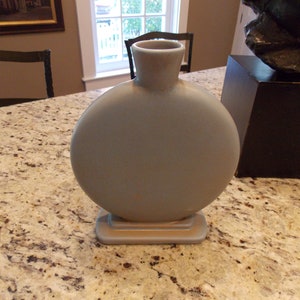 May include: A round, light blue ceramic vase with a wide base and a narrow neck. The vase is sitting on a granite countertop.