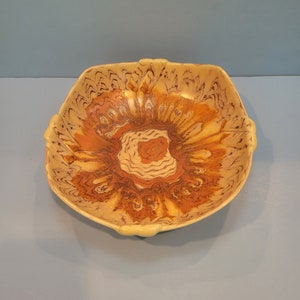 May include: A square ceramic bowl with a yellow glaze and brown and orange marbling. The bowl has a unique, abstract design.