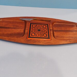 May include: A wooden serving tray with three compartments. The center compartment has a black and orange tile with a geometric design. A small knife is included.