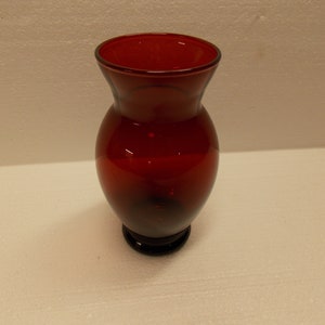 May include: A deep red glass vase with a rounded body and a flared top. The vase has a small, round base.