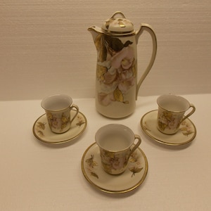 May include: A vintage porcelain coffee set with a floral design. The set includes a coffee pot, three cups, and three saucers. The cups and saucers have a gold trim.