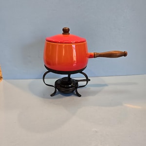 May include: Orange and red enamel fondue pot with a wooden handle and a black metal stand.