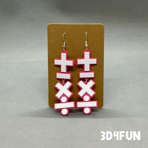 May include: A pair of pink dangle earrings featuring white mathematical symbols. The symbols are a plus sign, an equals sign, a multiplication sign, and a division sign. The earrings are displayed on a brown card with the text "3D4FUN".