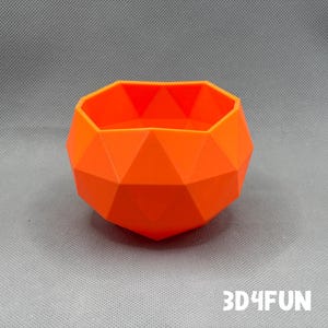 May include: Orange geometric planter with a faceted design. The planter is made of plastic and has a smooth finish.