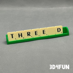 May include: A green plastic rack holds seven letter tiles spelling out the word "THREED".