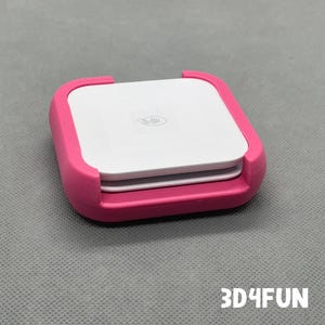 May include: A pink plastic case with a white square device inside. The device has a logo on it. The case is designed to hold the device securely.