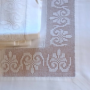 May include: White crocheted bed sheet with a delicate floral pattern. The sheet has a border of intricate crochet lace.