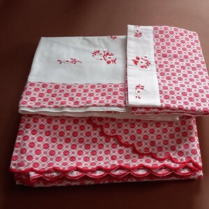 Peut inclure: Un ensemble de literie en coton blanc avec des broderies florales rouges. Le drap-housse a un bord festonné et un motif géométrique rouge et blanc.