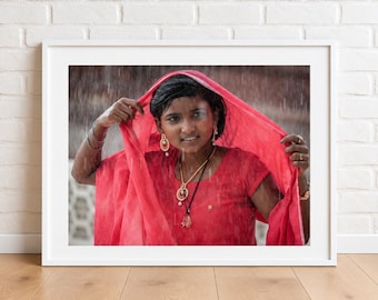 Puede incluir: Una fotografía enmarcada de una persona con un pañuelo rojo brillante y una parte superior a juego, adornada con joyas doradas que incluyen pendientes colgantes y un collar de varias capas, capturada al aire libre bajo una lluvia visible.