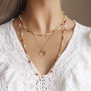 Peut inclure: Ensemble de colliers superposés à trois rangs. Le rang supérieur est orné de petites perles rouges et de barres dorées, le rang du milieu d'un pendentif en forme de goutte et le rang inférieur de perles rouges et de perles. Les colliers sont de couleur or.