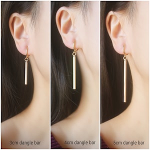 May include: Three gold dangle bar earrings with different lengths: 3 cm, 4 cm, and 5 cm. The earrings are shown on a model's ear.