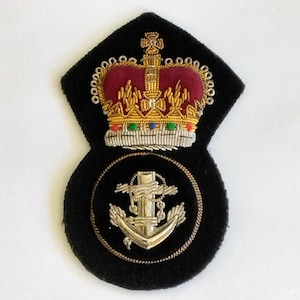 May include: A black embroidered patch featuring a gold and red crown above a circular emblem with a silver anchor. The anchor is surrounded by a gold rope design. The patch is likely a military or nautical insignia.