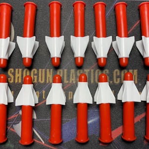 May include: A set of 15 red and white plastic toy rockets. The rockets are about 3 inches long and have a white fin design.