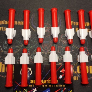 May include: Twelve red and white plastic toy missiles. The missiles are about 3 inches long and have a white nose cone and red body. The missiles are arranged in two rows of six.
