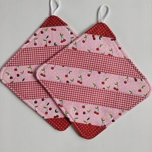 Könnte beinhalten: Zwei rosa und rote gequiltete Topflappen mit einem Kirschendruck und weißen Gingham-Streifen.