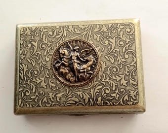 May include: Rectangular metal case with an ornate, swirling pattern and a central medallion featuring a winged figure riding two horses. The case has a bronze and silver color scheme.