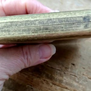 May include: A rectangular, antique brass-colored box with a hinged lid. The box has a slightly worn appearance, suggesting age and use. The surface shows subtle variations in color and texture.