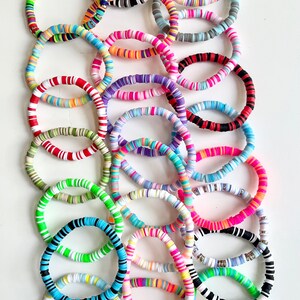 May include: A collection of colorful bracelets made of stacked, round, plastic beads. The bracelets are in various colors and patterns, including black, white, red, green, blue, pink, and yellow.