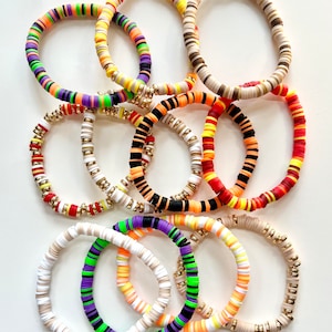 May include: A set of colorful bracelets made with stacked, round, plastic beads. The bracelets feature a variety of color combinations, including black and orange, red and orange, white and orange, and purple and green. Each bracelet has a gold accent.