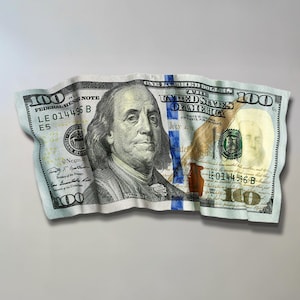 May include: A crumpled $100 bill with a portrait of Benjamin Franklin. The bill is partially obscured by a blue and white stripe. The bill has the text "FEDERAL RESERVE NOTE" and "UNITED STATES OF AMERICA" printed on it.
