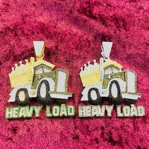 Könnte beinhalten: Zwei Anhänger aus Gold und Silber mit einem LKW-Design, mit einer Krone oben und den Worten "Heavy Load" in grünen und weißen Buchstaben.