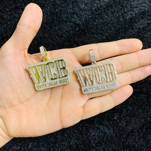 May include: Two gold pendants with the text "WCB White Collar Bosses" set with clear cubic zirconia stones.