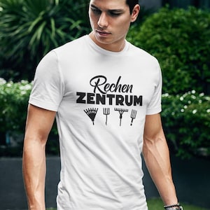 Könnte beinhalten: Weißes T-Shirt mit dem schwarzen Text "Rechen ZENTRUM" und Illustrationen von Gartengeräten. Das Model trägt eine blaue Jeans. Das T-Shirt ist kurzärmlig.