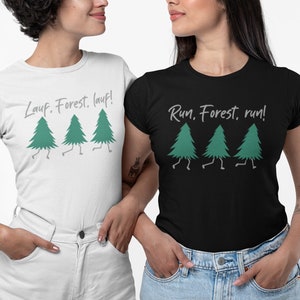 Könnte beinhalten: Zwei T-Shirts, eines weiß und eines schwarz, jeweils mit einer grünen Baumgrafik mit Beinen und den Sätzen "Lauf, Forest, lauf!" und "Run, Forest, run!". Die Shirts werden von zwei Personen getragen.